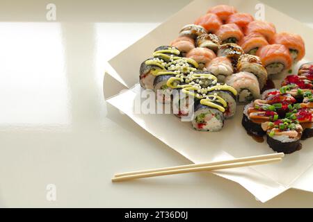 Leckere Sushi-Rollen in Einweg-Papierkarton auf weißem Tisch. Lieferservice Japan Food im Öko-Container-Konzept Stockfoto