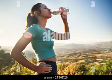 Durstige Frau trinkt Wasserflasche an sonnigem Tag Stockfoto