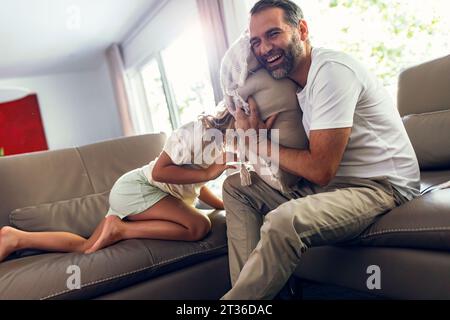 Der glückliche Vater spielt gern mit der Tochter auf dem Sofa Stockfoto