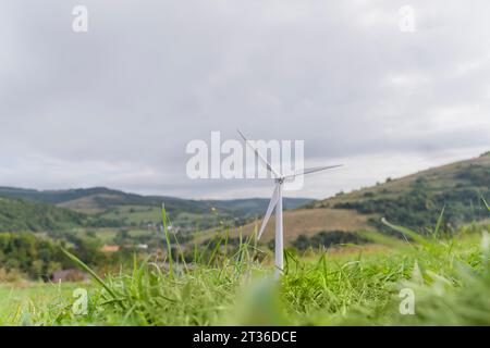 Windturbinenmodell auf Gras unter bewölktem Himmel auf der Wiese Stockfoto