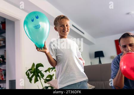 Lächelnder Junge mit Ballon, der zu Hause beim Vater steht Stockfoto
