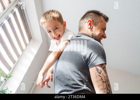 Verspielter Vater, der zu Hause den Sohn auf der Schulter trägt Stockfoto