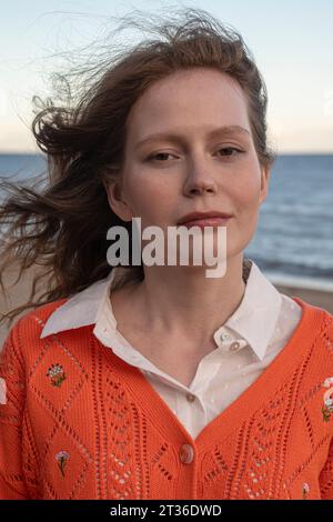 Eine junge Frau, die am Strand einen orangefarbenen Pullover trägt Stockfoto