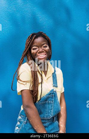 Glückliche junge Frau mit Vitiligo, die vor einer blauen Wand steht Stockfoto