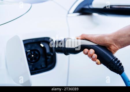 Eine Frau, die ein Ladegerät in einem Elektroauto an der Station anschließt Stockfoto