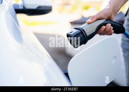 Hand einer Frau, die den Stecker in der Nähe eines Elektroautos hält Stockfoto