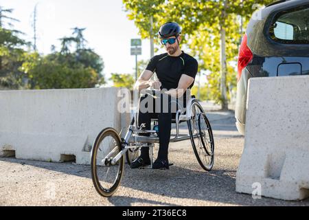 Sportler mit Sonnenbrille sitzt im Rollstuhl auf der Straße Stockfoto