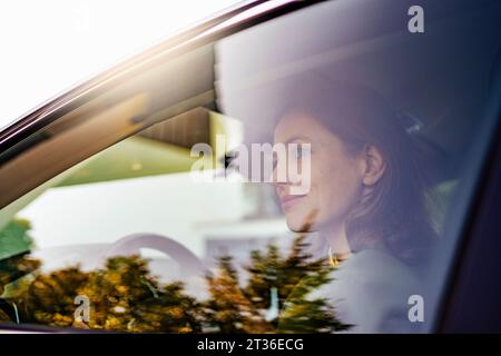 Lächelnde Frau, die ein Elektroauto fährt, durch das Fenster gesehen Stockfoto