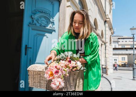Frau, die frischen Blumenstrauß in den Fahrradkorb an sonnigem Tag legt Stockfoto
