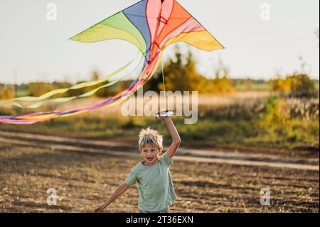 Verspielter Junge, der mit mehrfarbigem Drachen auf der Wiese läuft Stockfoto