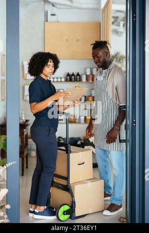 Eine Frau, die die Zwischenablage hält und mit dem Kellner im Café spricht Stockfoto