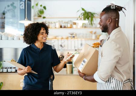 Lächelnde Frau, die den QR-Code aus dem Paket im Café scannt Stockfoto