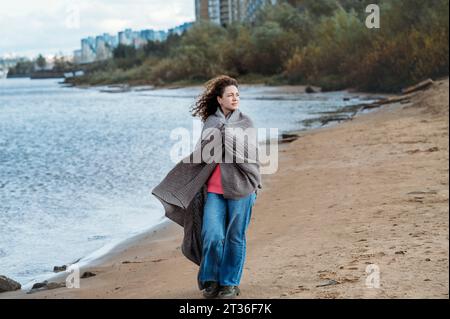 Frau, die in einen Schal gehüllt ist und am Strand läuft Stockfoto