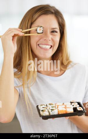 Eine verspielte junge Frau, die eine Sushi-Rolle hält Stockfoto