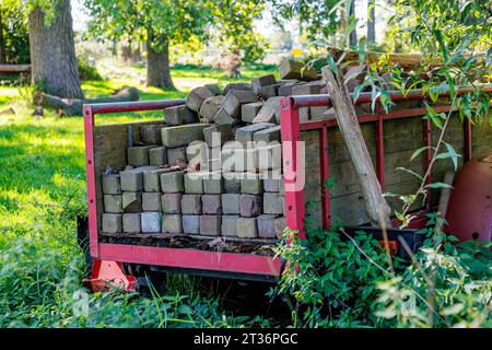 Rustikaler Wohnwagen mit Ziegeln und zwei Baumstämmen zwischen verlassener grüner, wilder Vegetation im Hinterhof einer Farm, Bäume und Sonnenlicht im verschwommenen Hintergrund, Sonne Stockfoto