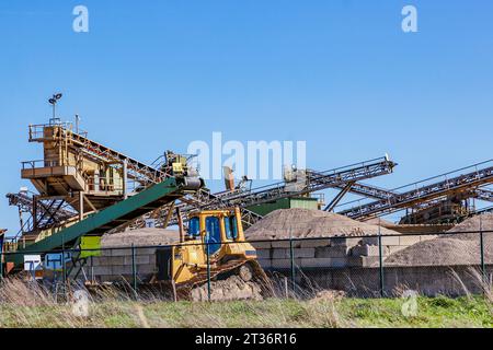 Baustelle für Kies-, Sand- und Erdgewinnung, Maschinen für schwere industrielle Extraktion, Förderband, Brecher und Kies sortieren, blauer Himmel im Hintergrund, Stockfoto