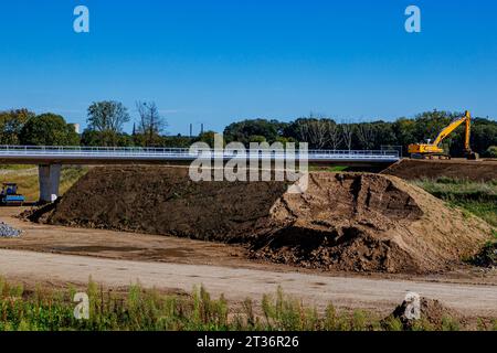 Ansammlung von Sand im Straßenbau- und Reparaturbereich, Brücke im Bau, Raupenbagger, Laubbäume vor blauem Himmel im Hinterland Stockfoto