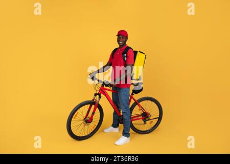 Positiver, selbstbewusster Millennial Black man Kurier in Uniform mit Rucksackfahrten auf dem Fahrrad Stockfoto