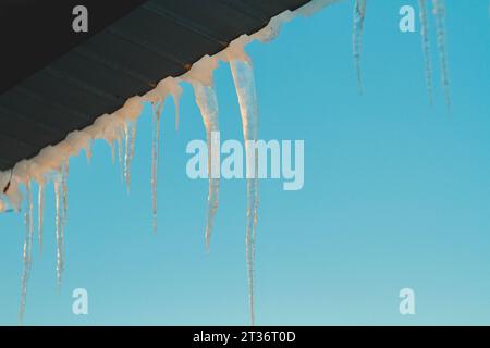 Das Schmelzwasser fließt vom Dach . Eiszapfen auf dem Dach des Hauses. Wunderschönes Eis im Winter... Stockfoto