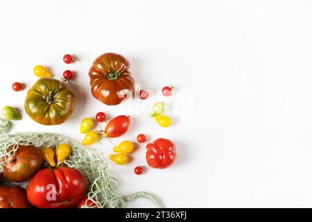 Rote, grüne, gelbe und gestreifte Tomaten in einem Schnur-Beutel auf einem grauen Tisch mit Platz für Text. Flache Lagen. Gesundes Essen, frisches gesundes Gemüse aus dem Stockfoto