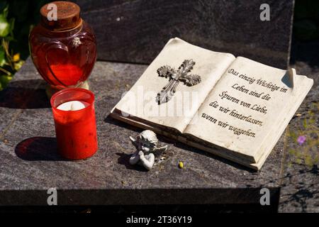 Auf dem Grabstein befindet sich eine Engelsfigur und ein Buch mit Text in deutscher Sprache, und in der Nähe stehen rote Lampen. Stockfoto