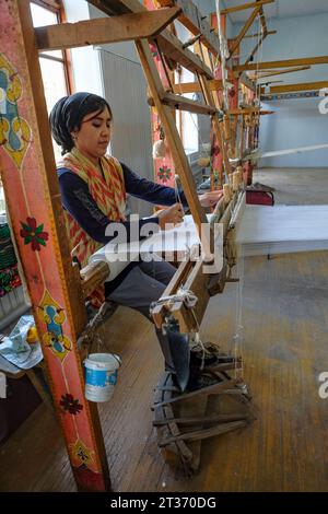 Margilan, Usbekistan - 20. Oktober 2023: Eine Frau, die mit Seide auf einem Webstuhl in Margilan, Usbekistan, arbeitet. Stockfoto