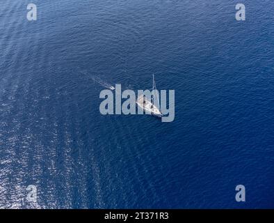 Ein Segelboot segelt und schleppt ein kleines aufblasbares Boot auf einer blauen Meeresluftdrohne, die von oben geschossen wird Stockfoto