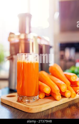 Ein Glas frisch gepressten Karottensaft, Karotten und Saftpresse in der Küche Stockfoto