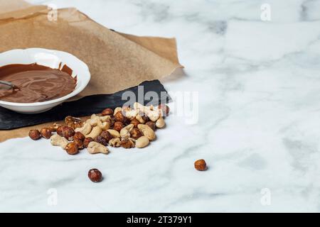 Schokoladenglasur in weißer Schüssel auf Backpapier, Nussmischung, Kopierraum Stockfoto