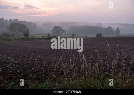 nebliger Sonnenuntergang, gepflügtes Feld, Sonnenuntergang über dem gepflügten Feld, romantische traumhafte Landschaft Stockfoto