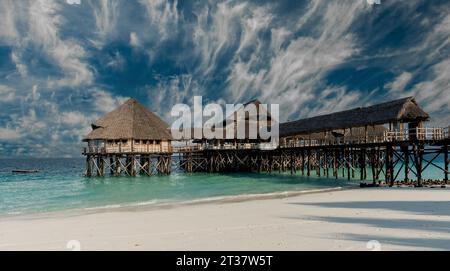 Wunderschöner Blick auf den Holzpier mit Strohhütten im Meer vom Sandstrand in Sansibar Stockfoto