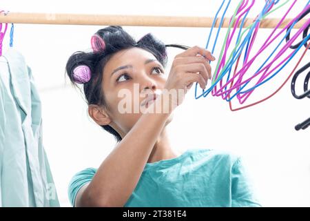 Eine junge Frau mit Lockenwicklern im Haar hängt nasse Wäsche an Kleiderbügel Stockfoto