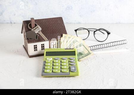 Hausmodell, Schlüssel, Geld und Taschenrechner auf weißem Tisch Stockfoto