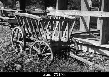 Ein hölzerner Bauernwagen parkt vor einem alten Schuppen in der Sommersonne. Das Bild wurde auf analogem Schwarzweißfilm aufgenommen. Stockfoto