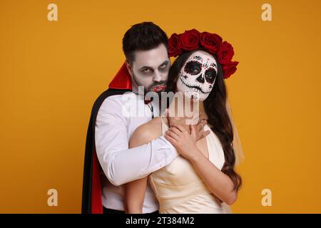 Ein Paar in gruseligen Braut- und Vampirkostümen auf orangem Hintergrund. Halloween-Feier Stockfoto