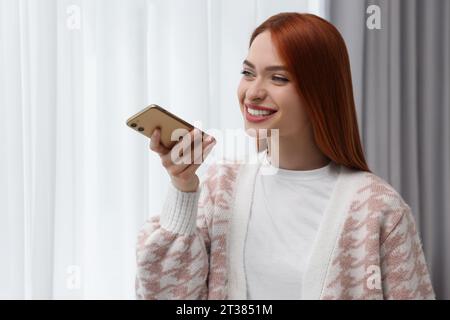 Glückliche Frau, die zu Hause eine Sprachnachricht per Smartphone sendet Stockfoto