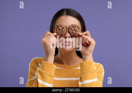 Junge Frau mit Schokoladenchips-Keksen auf lila Hintergrund Stockfoto