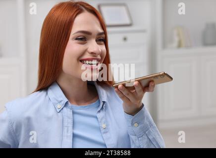 Glückliche Frau, die zu Hause eine Sprachnachricht per Smartphone sendet Stockfoto