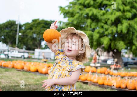 Ein kleines Mädchen mit Strohhut wählt Kürbisse auf dem Kürbisfeld auf einer Farm. Familientraditionen im Herbst Stockfoto