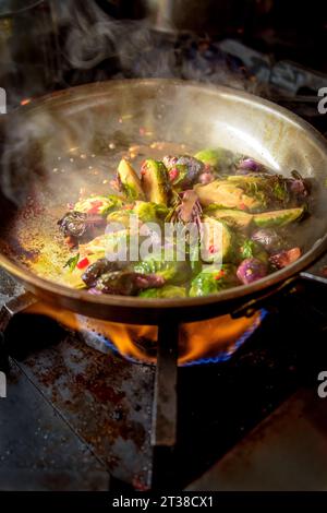 Grüne und violette Rosenkohl werden in einer Pfanne mit Flammen gekocht Stockfoto