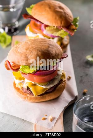 Frisch zubereitete Cheeseburger auf Servierplatte mit Speck, Salat, Tomaten, Zwiebeln und Gurken Stockfoto