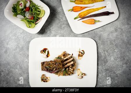 Lamm mit Wildreis, Karotten, Salat und Pilzen auf dem Tisch Stockfoto