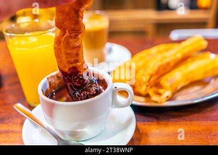 Typische spanische Frühstücks-Churros, die in heiße Schokolade mit Orangensaft und Kaffee in Sevilla, Spanien, getaucht werden Stockfoto