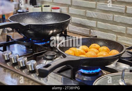 Hälften frischer Aprikosen werden in Karamellsirup in einer Pfanne auf einem Gasherd gebraten Stockfoto