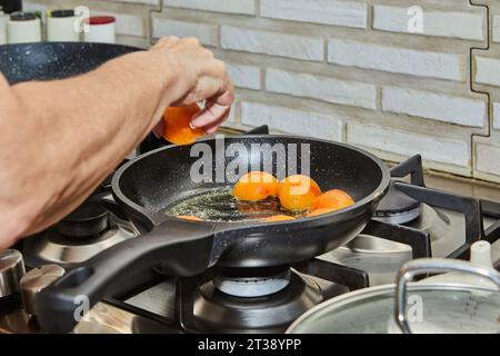 Hälften frischer Aprikosen werden in Karamellsirup in einer Pfanne auf einem Gasherd gebraten Stockfoto