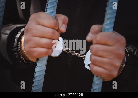Handschellen eines Gefangenen hinter Gittern eines Gefängnisses. Der Begriff der Unfreiheit. Ein Gefangener in einem Gefängnis oder Gerichtssaal mit Handschellen. Stockfoto