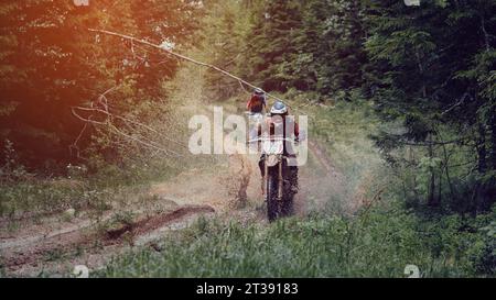 Motorradrennfahrer auf Enduro-Sport Motorradfahrer fahren auf einer matschigen Straße mit Pfützen im Wald bei einem Off-Road-Rennen an sonnigen Tagen Stockfoto