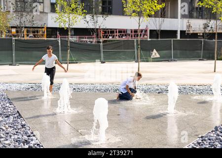 Süße junge Schwestern, die in Springbrunnen spielen. Kinder, die an sonnigen Sommertagen Spaß mit Wasser haben. Aktive Freizeit für Kinder. Stockfoto