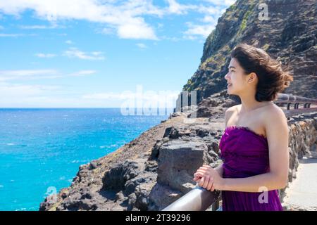 Junge Frau in formellem lila Kleid am Makapu'u Aussichtspunkt mit Blick auf den Makapu'u Strand und den hawaiianischen Ozean auf Oahu, Hawaii Stockfoto