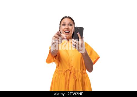 Junge freundliche brünette Frau in einem gelben Sommerkleid macht ein Foto am Telefon Stockfoto